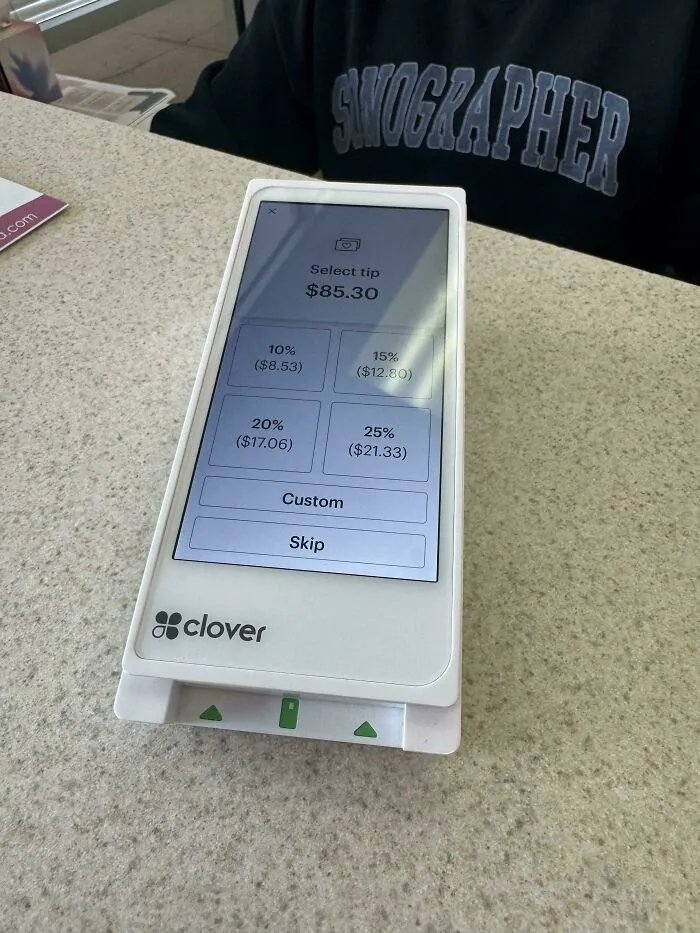 A Clover payment terminal displaying options to select tip percentages, illustrating challenges in tipping culture.