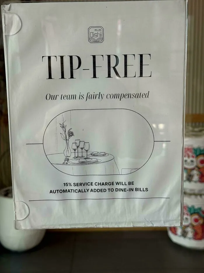 A sign indicating a restaurant is tip-free with a 15% service charge, highlighting the tipping culture.