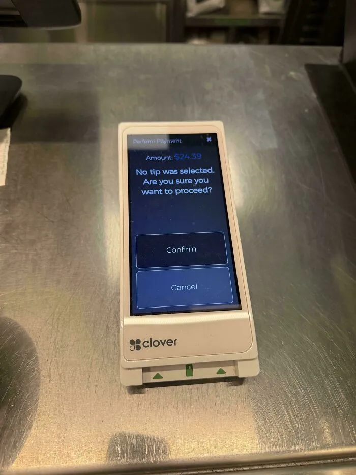 A Clover payment device showing an amount and asking to confirm no tip was selected, impacting tipping culture.