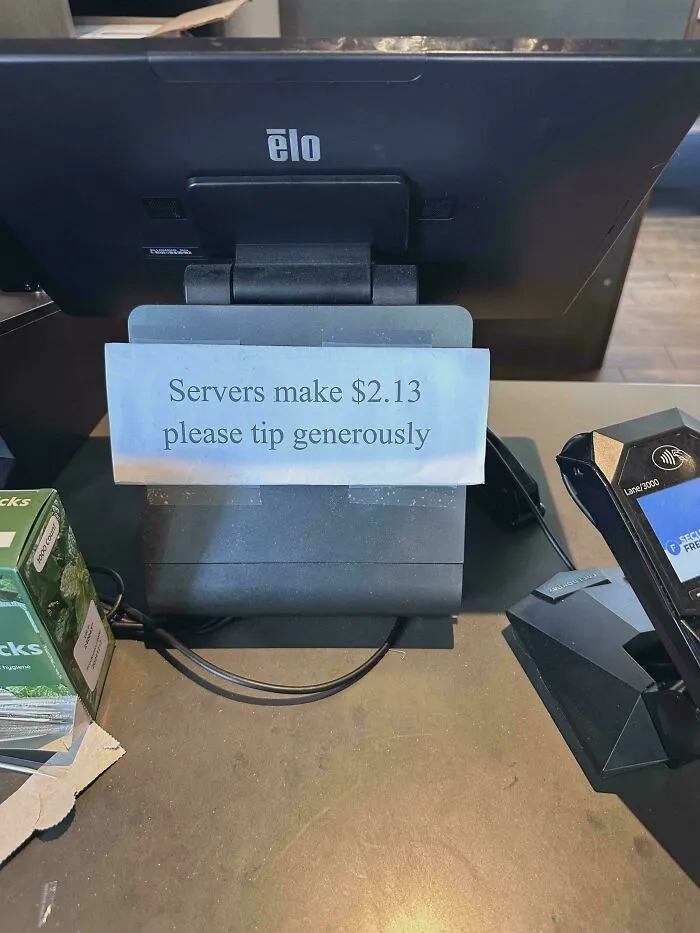 A sign at a point-of-sale system that reads Servers make $2.13 please tip generously, reflecting tipping culture.