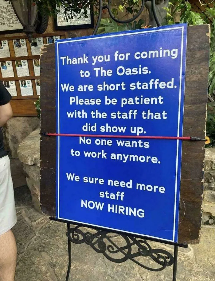 A sign at a restaurant called The Oasis asking for patience due to being short-staffed and needing more staff, relating to the challenges of tipping culture.