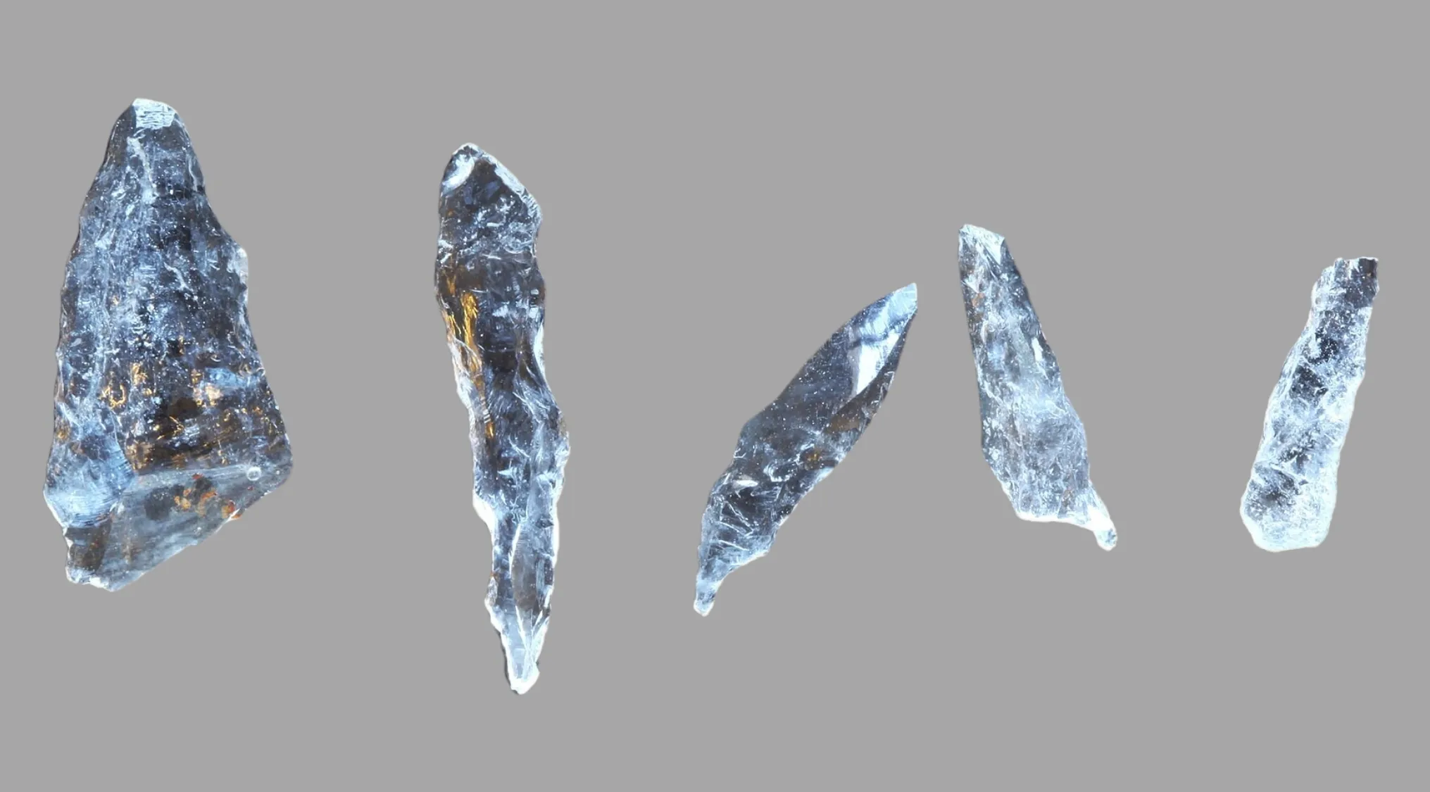 Five translucent, sharp ancient tools or microliths, used for various purposes, displayed against a gray background.