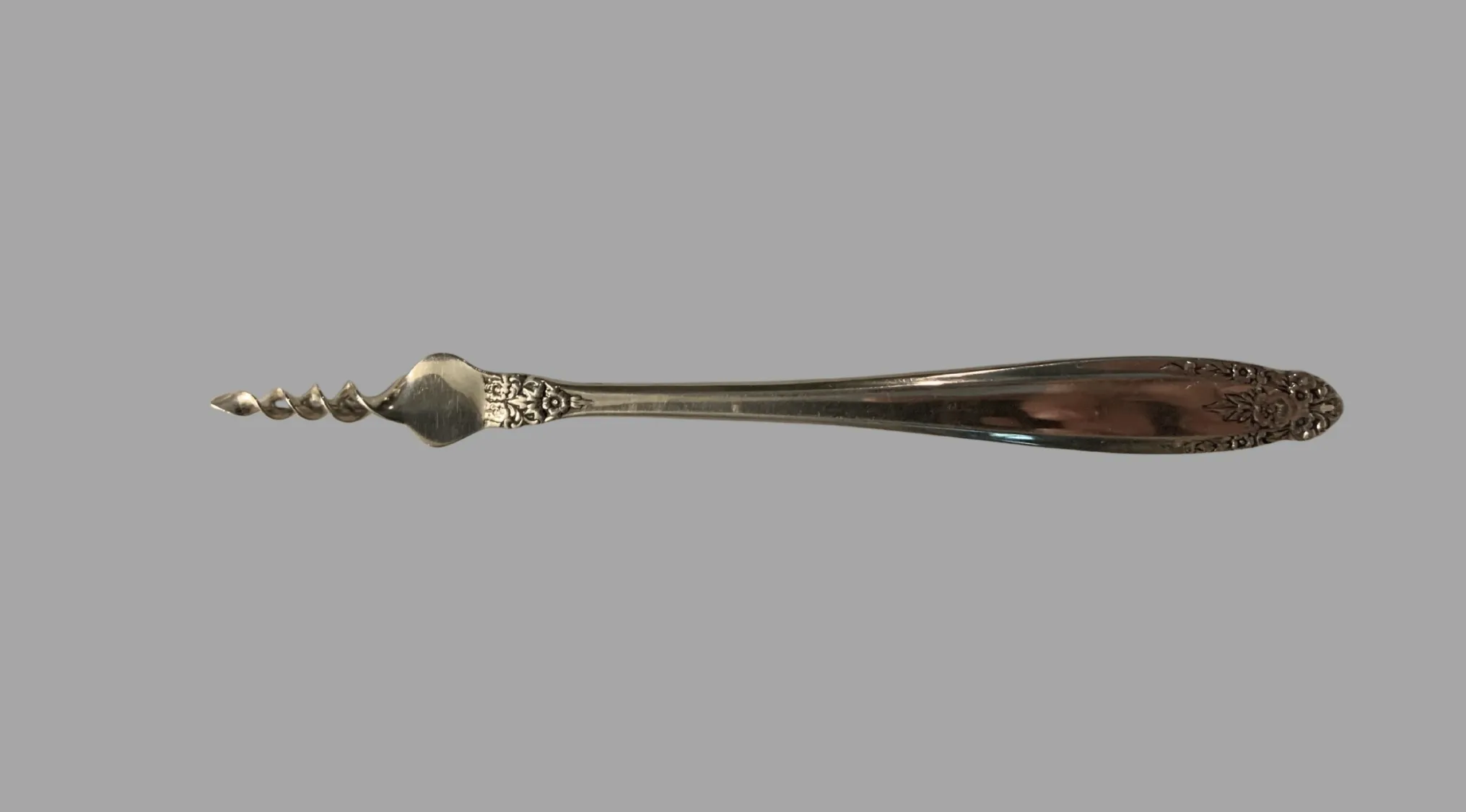 A detailed close-up of a vintage silver tool with a corkscrew end and an ornate handle on a grey background. Ancient Tools.