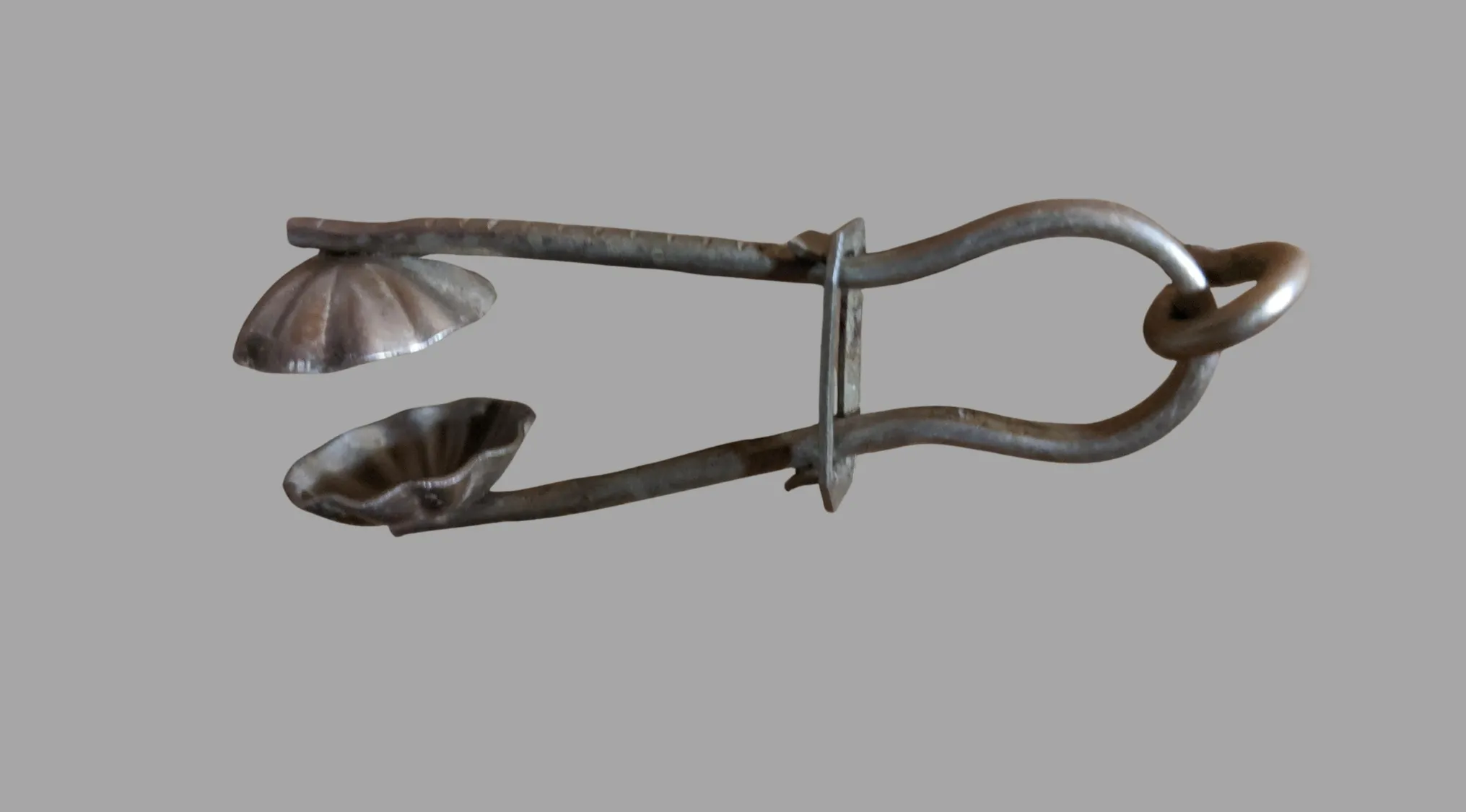 A metallic ancient household item, resembling tongs with shell-shaped cups, on a gray background, revealing its ancient tools nature.
