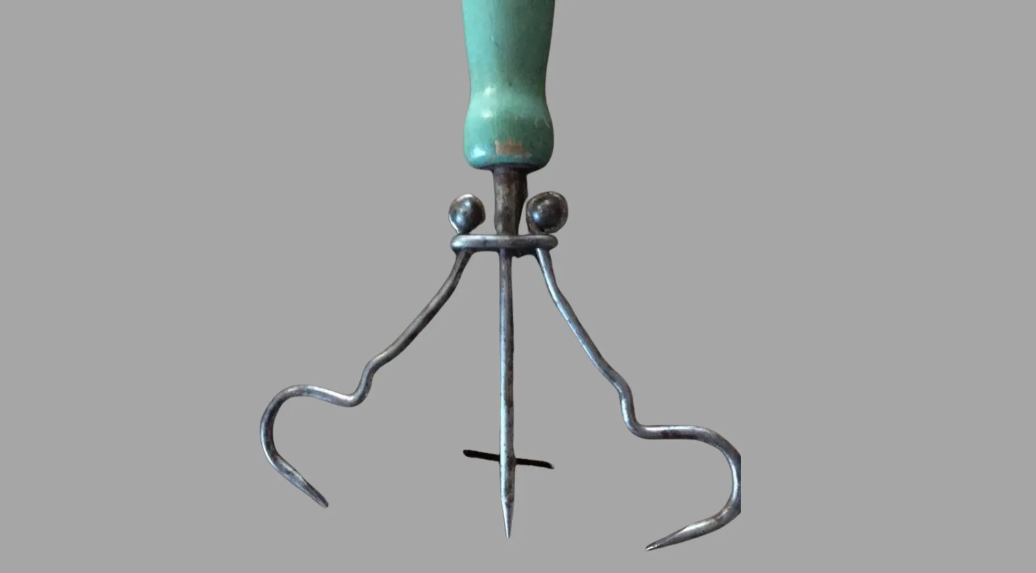 An antique tool with a green wooden handle and three curved metal prongs, an example of ancient tools.