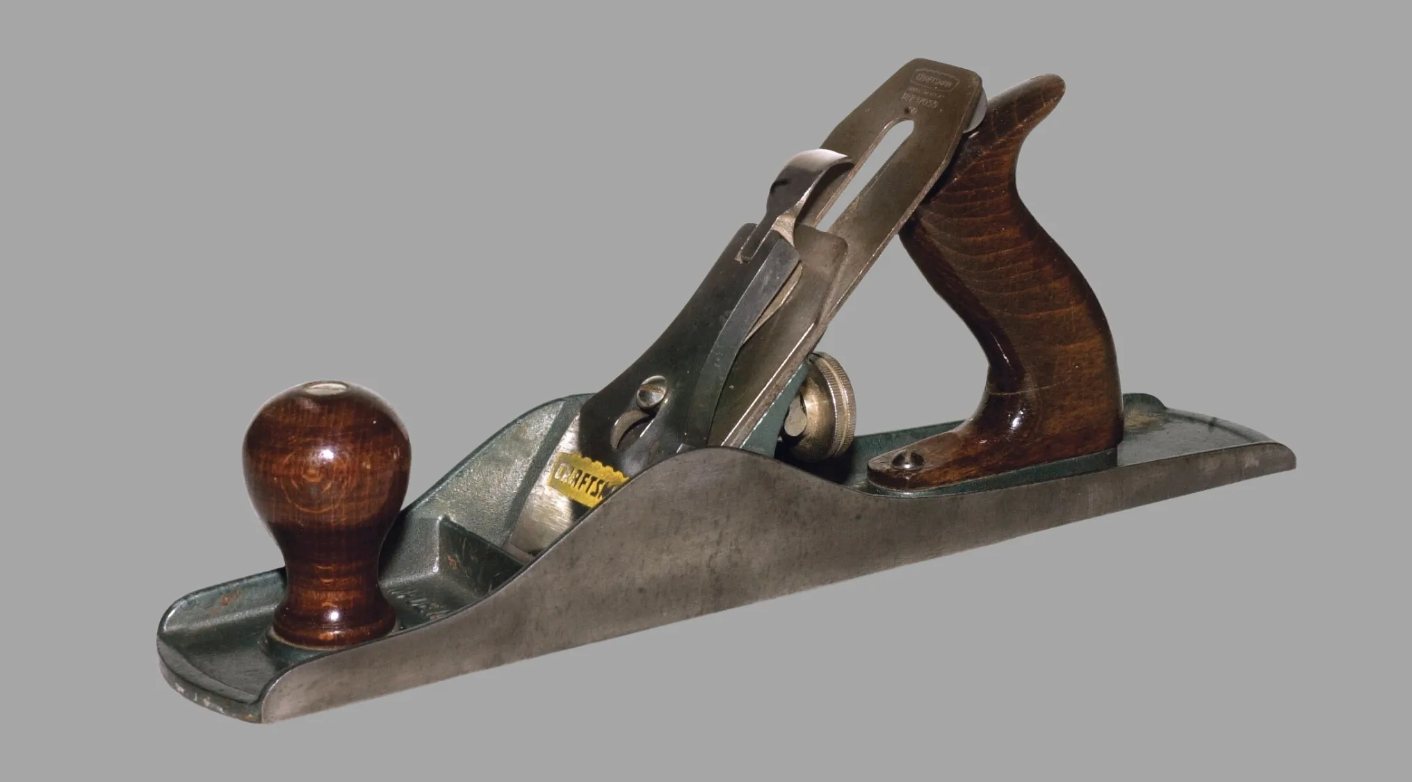 A close-up of a hand plane, an ancient tool for woodworking, with a dark wooden handle and a metal blade.