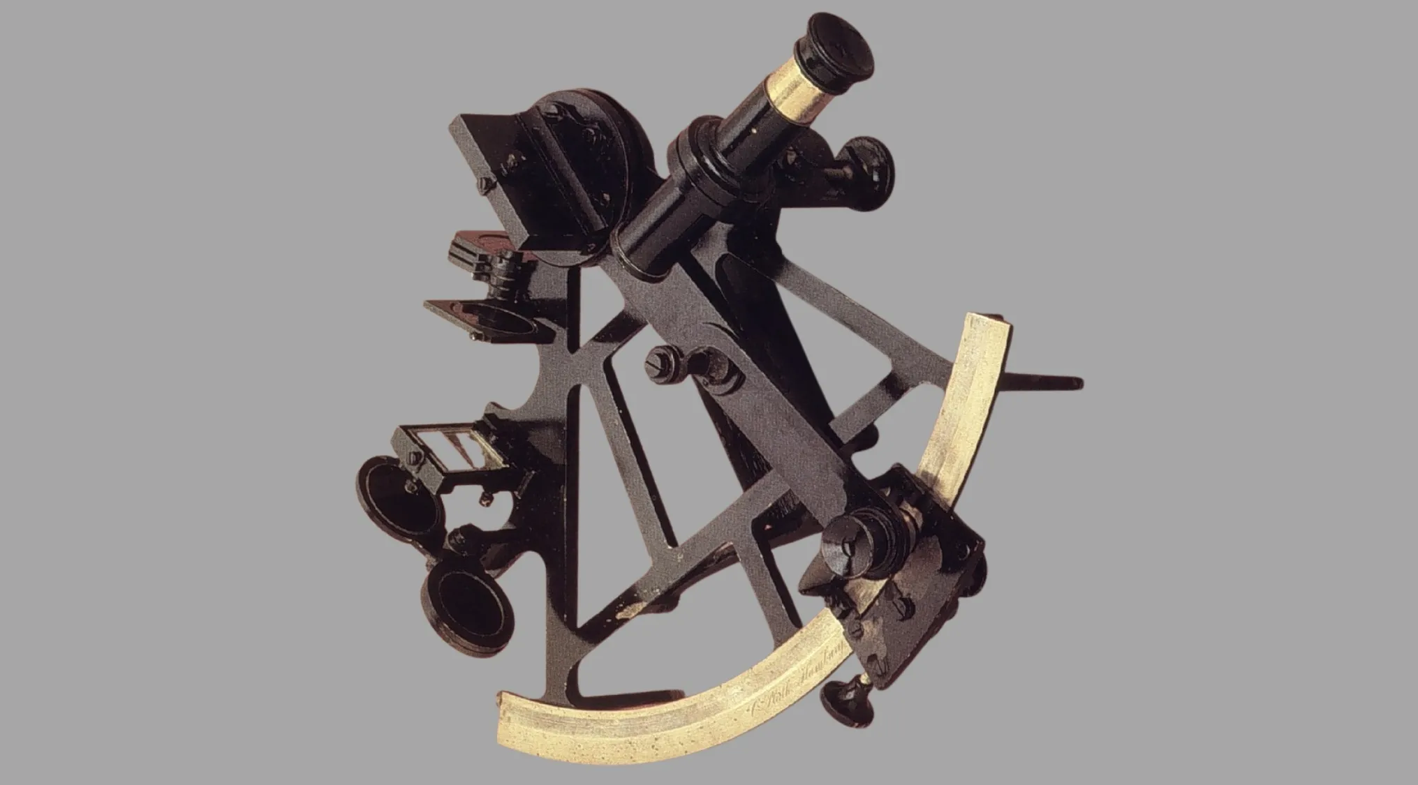 A black and brass sextant, an ancient tool, stands on a gray background. Its purpose is navigation.