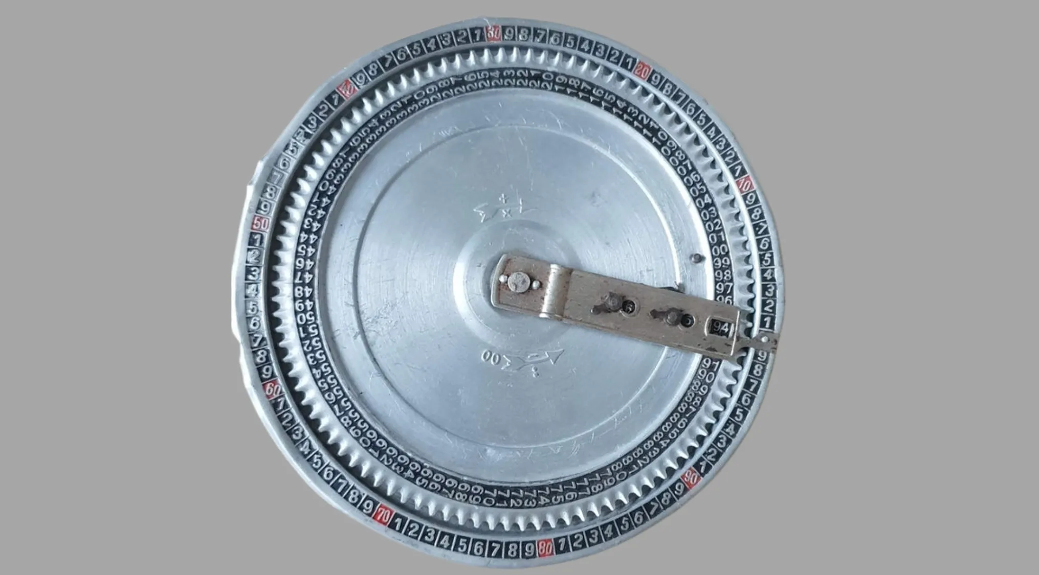 A close-up of an ancient tool, a circular metallic device with numbers and a central pointer. Identify purpose.