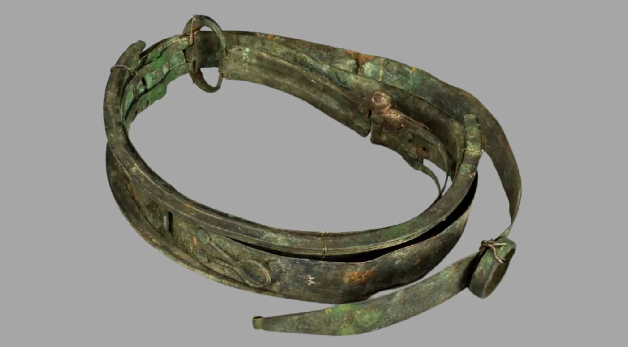 An ancient, tarnished copper medical tool, appearing as a segmented band with decorative elements, lies on a gray background.