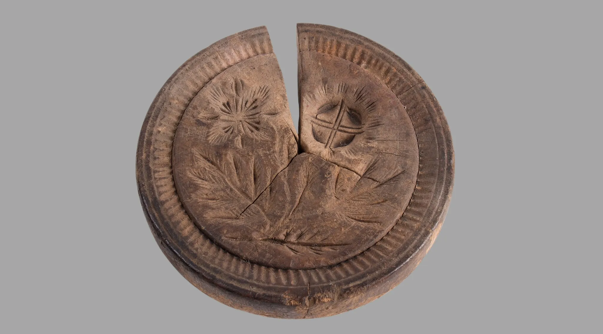 An antique wooden round tool, split down the middle with intricate floral and geometric carvings, showcasing ancient tools craftsmanship.