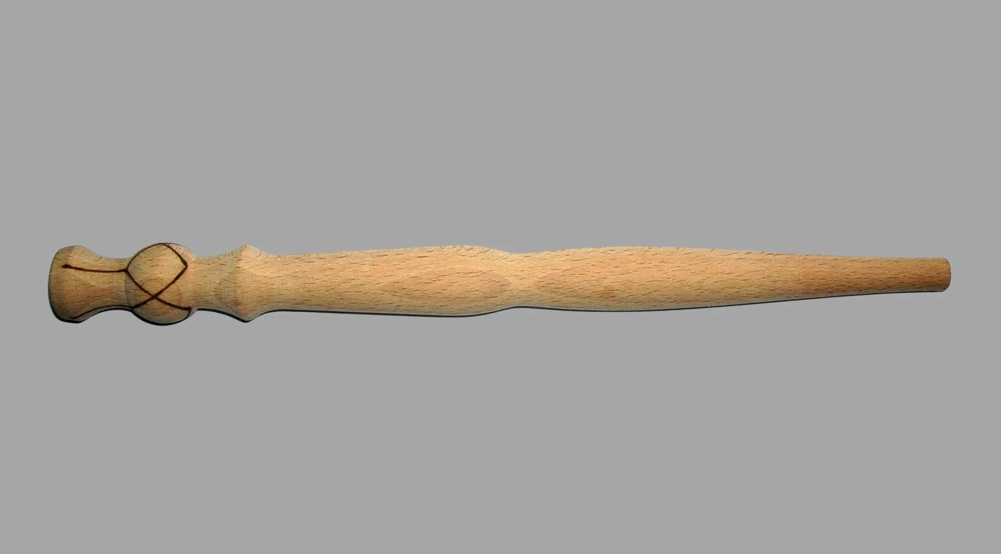 A light wooden spurtle, an ancient tool with a carved handle, against a grey background.