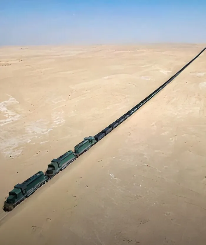 An extremely long train stretches across a vast, flat desert landscape, making it seem eerie and desolate.