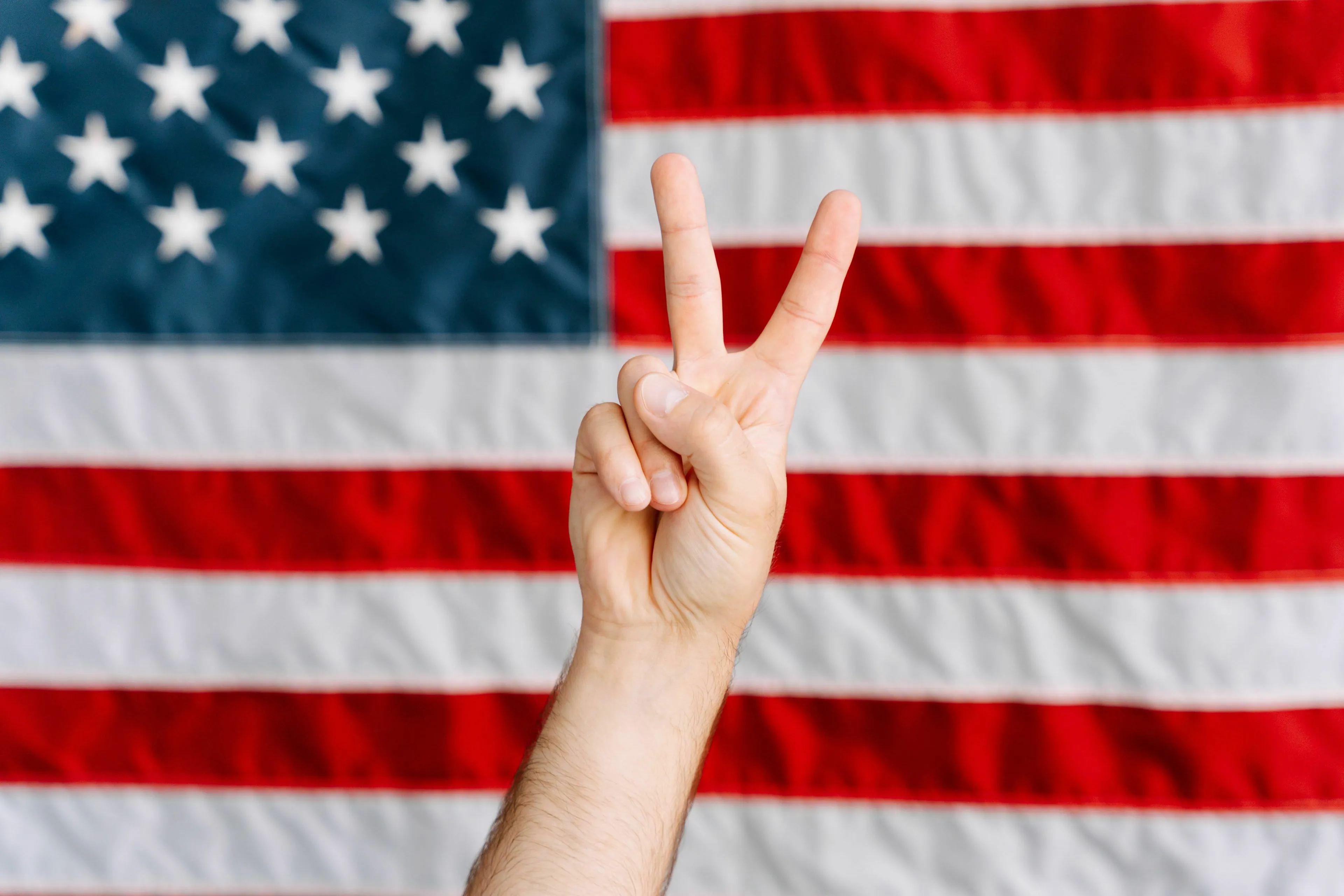 Hand showing peace sign in front of the US flag for US History and the 'American System'.