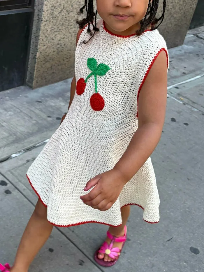 Child wearing a handmade crochet dress with cherry design in yarn