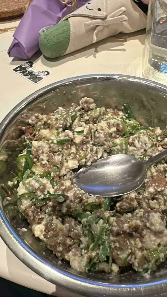 A metal bowl containing a unappealing mix of minced meat and green onions, a questionable food combo.