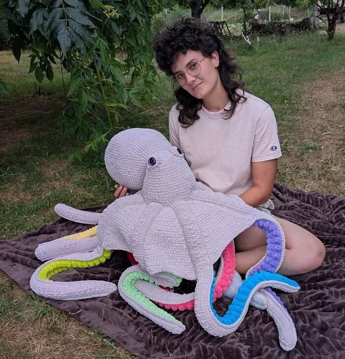 Person sitting outdoors with giant crochet octopus plush