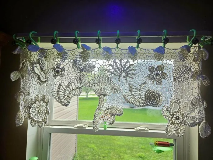 Intricate crochet lace curtain with floral designs hanging in window