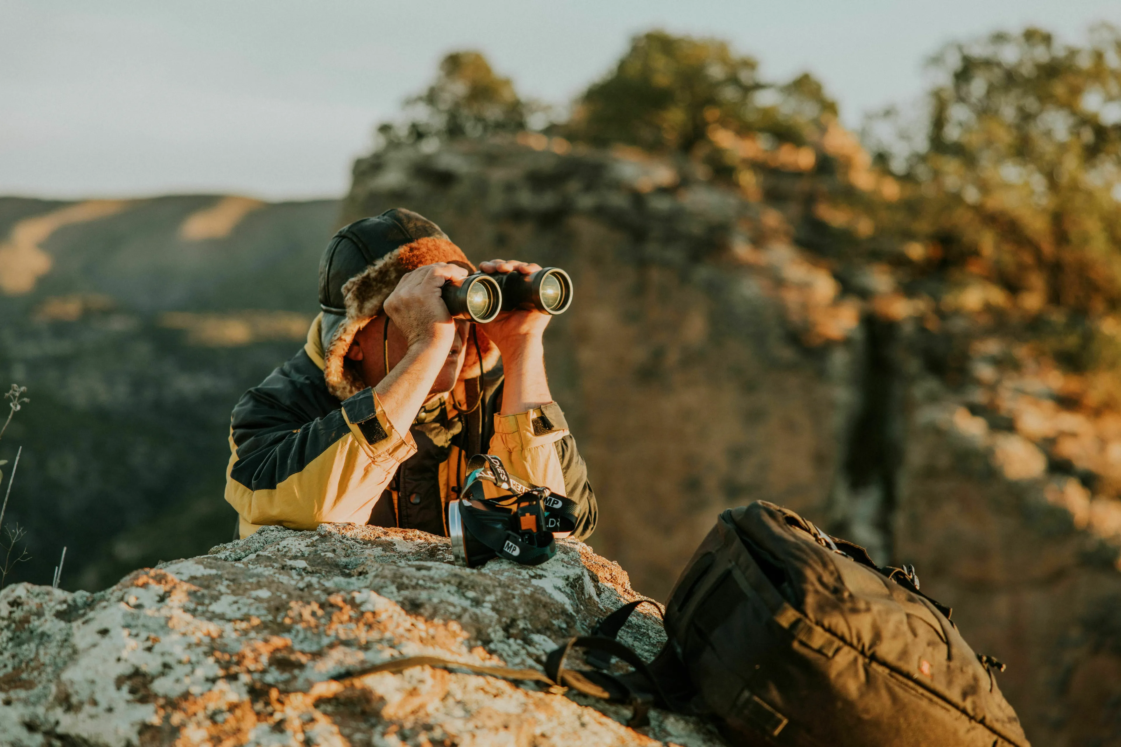 A person looking through binoculars from a rocky outcrop, symbolizing being watched constantly in Ancient Rome.