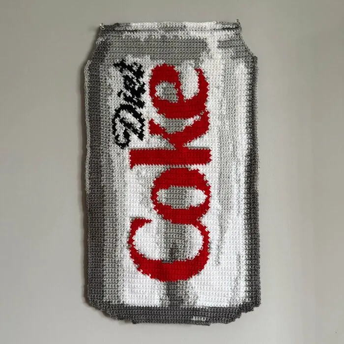 Crochet art of a Diet Coke can hanging on a wall