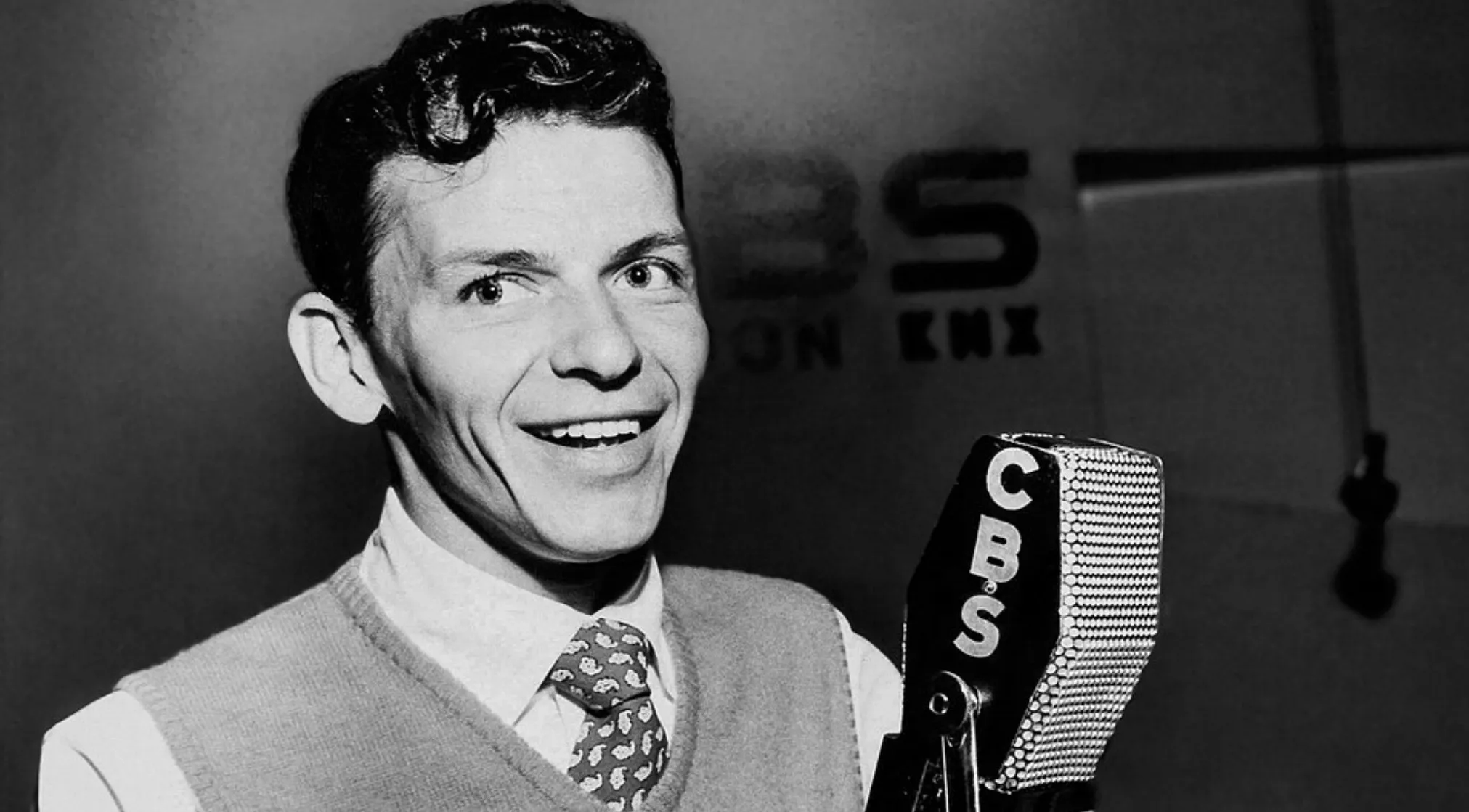 Black and white photo of Frank Sinatra smiling at a CBS microphone. Useless facts about movies and stars.