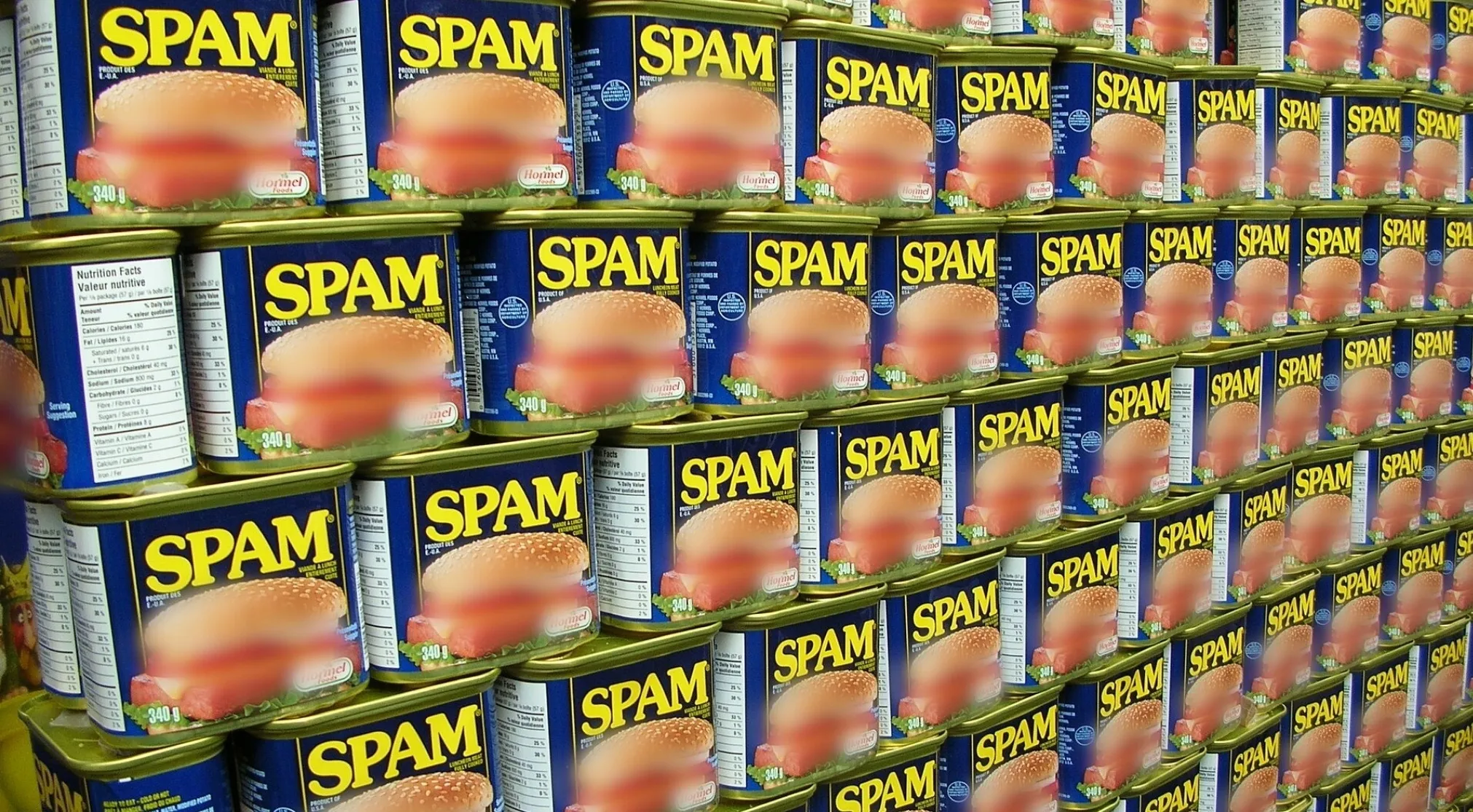 A wall of stacked Spam cans. The word Spam is the main keyword. Useless facts about what Spam is short for.
