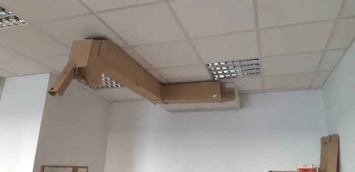 A wild and unhinged way to fix an air conditioner, using a cardboard duct extension on a ceiling.