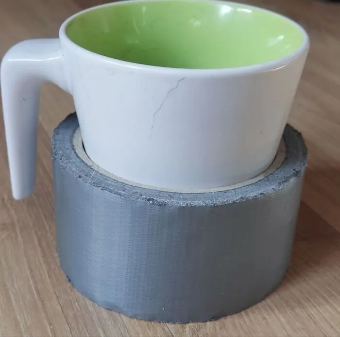 A white mug with a green interior placed on a roll of grey duct tape, a wild and unhinged fix.