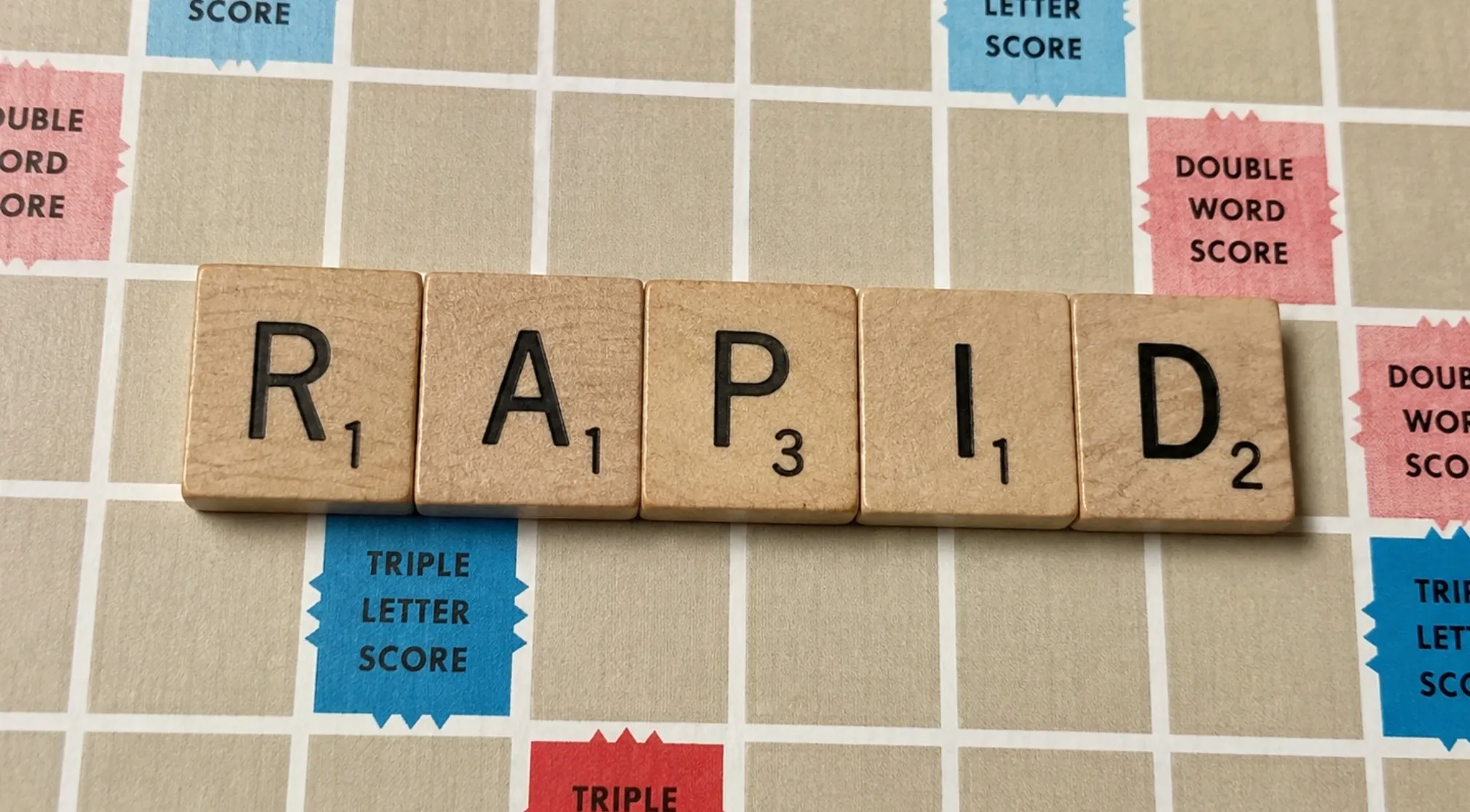 Scrabble tiles spelling RAPID on a board, illustrating a Chinese Exam Language concept with word scores.