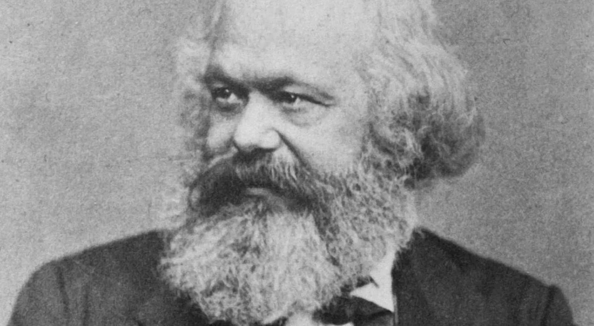 A historical black and white portrait of Karl Marx, a key figure in political science, with a prominent beard and mustache. The core value of Marxism is visible in his thoughtful expression.