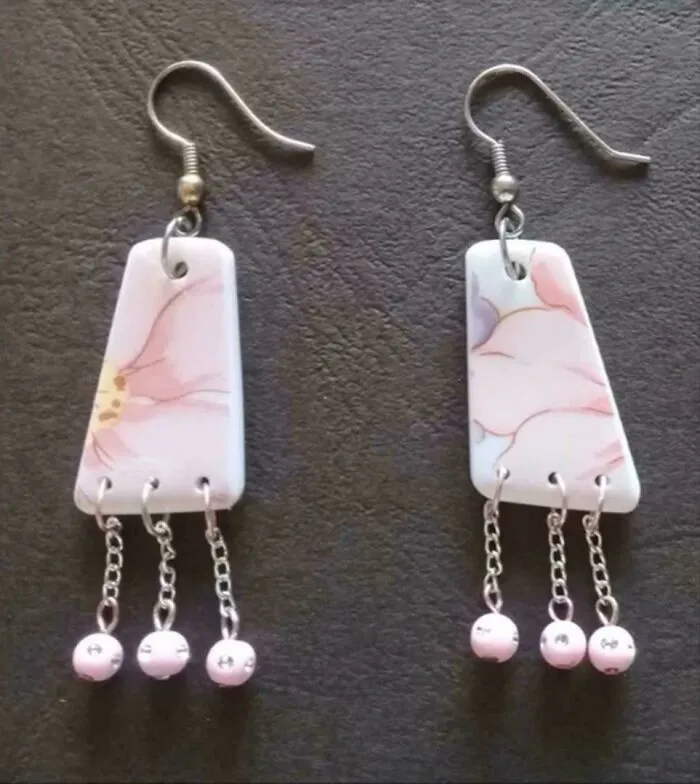 Close-up of earrings made from old junk, porcelain pieces with pink floral patterns and dangling beads.