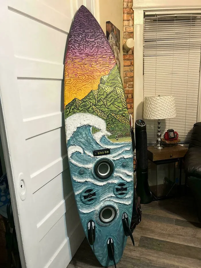An old junk surfboard repurposed into art, depicting a vibrant ocean scene with speakers integrated.