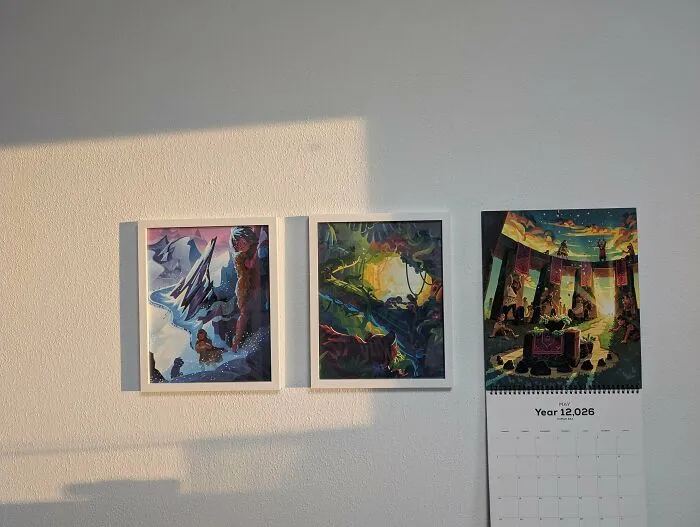 Three pieces of art and a calendar on a white wall, showcasing creativity.