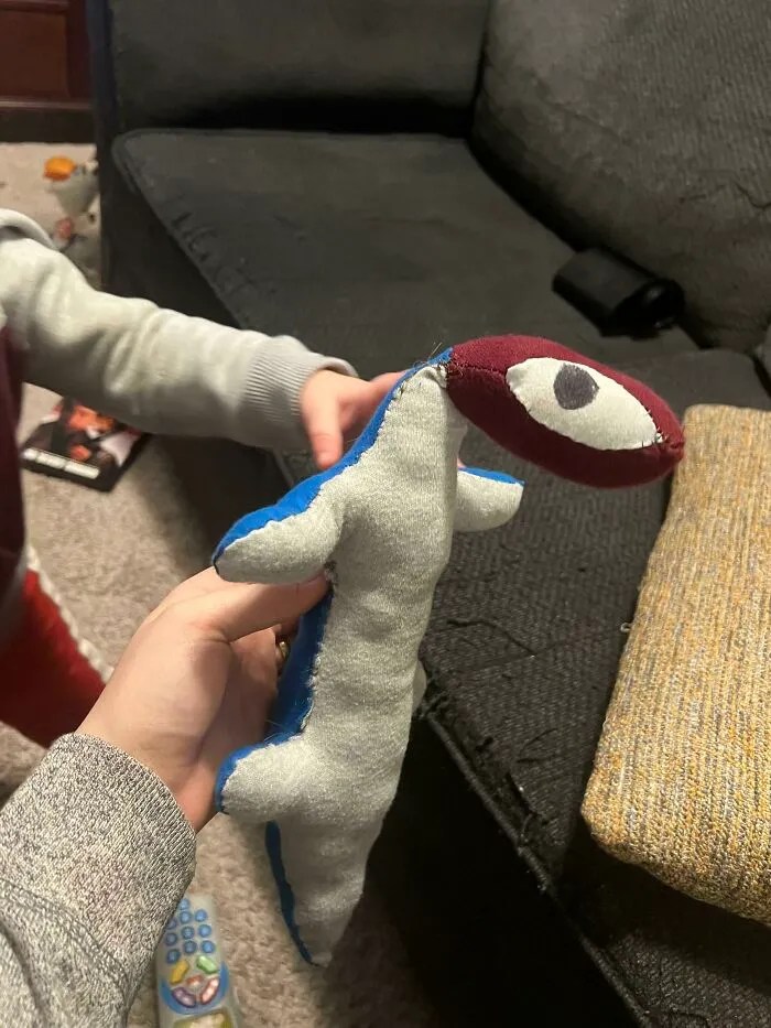 A handmade dinosaur plush toy, made from old junk, held in a child's hands, showcasing creativity.