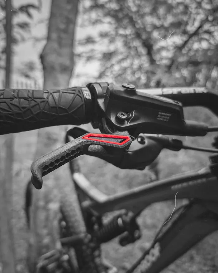 Amazing 3D printing creation: a custom brake lever with a red highlight on a mountain bike in grayscale.
