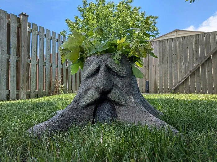 Amazing 3D printing creation: a tree stump planter with a face, holding green leaves, sitting in green grass.