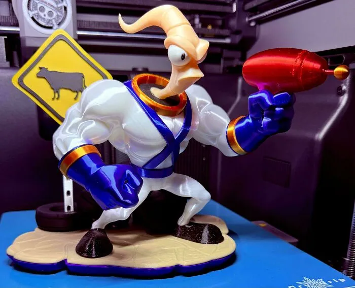 A detailed 3D printing creation of Earthworm Jim holding a ray gun, with a cow crossing sign, showing amazing craftsmanship.