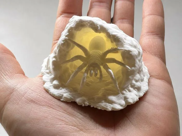 Amazing 3D printing creation of a glowing spider in its web held in a person's hand.