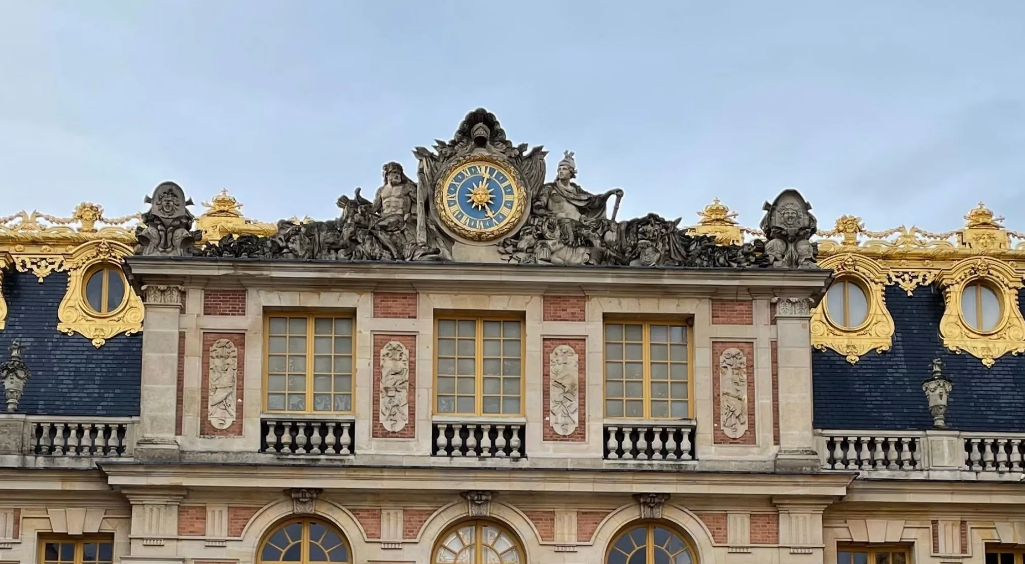A detailed view of the Palace of Versailles facade, featuring a central clock and ornate gold accents. World landmark.