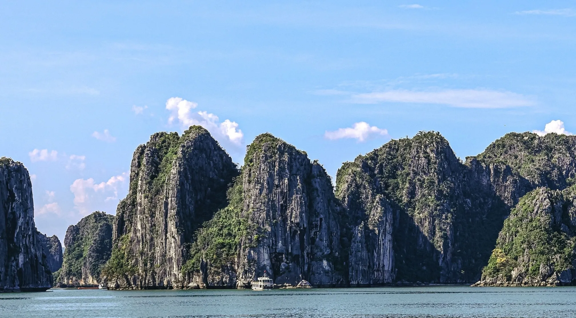 Guess the famous landmark: Majestic limestone islands rise from the turquoise sea under a clear sky, a boat visible near the base.