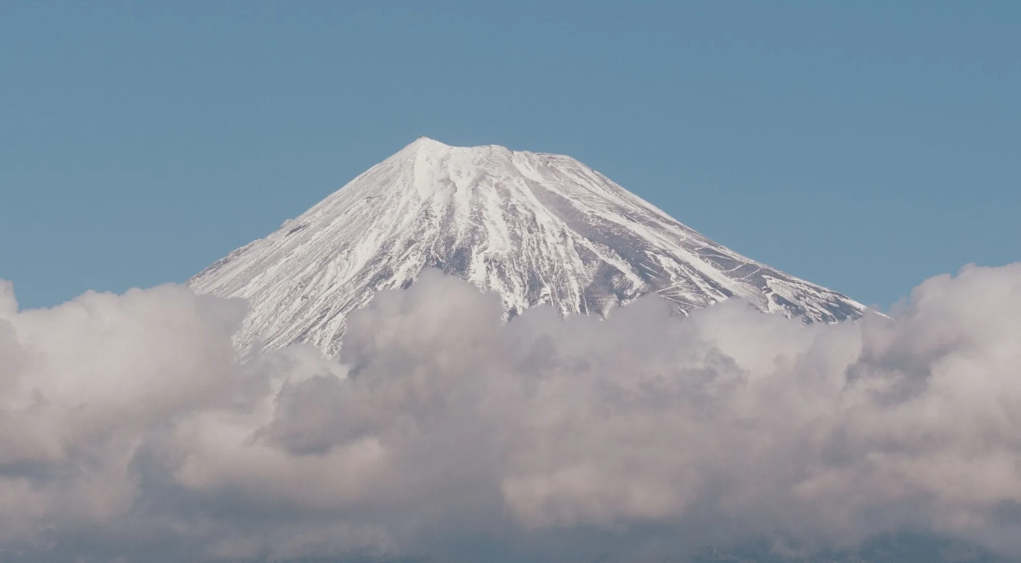 A Zoomed In Landmark: Majestic Mount Fuji, snow-capped peak rising above a sea of fluffy white clouds.