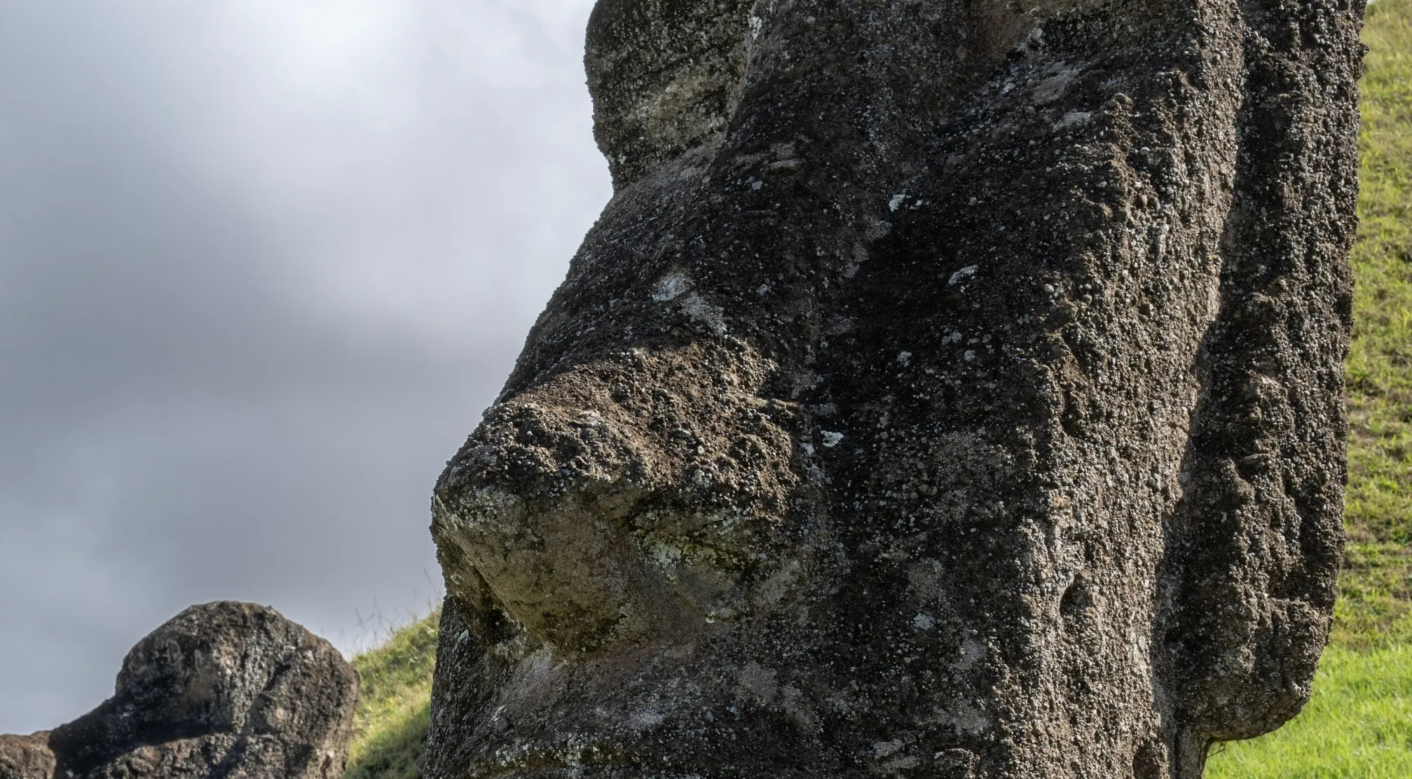 A close-up of a weathered stone Moai statue's nose and face, set against a cloudy sky. Zoomed in Landmarks challenge.