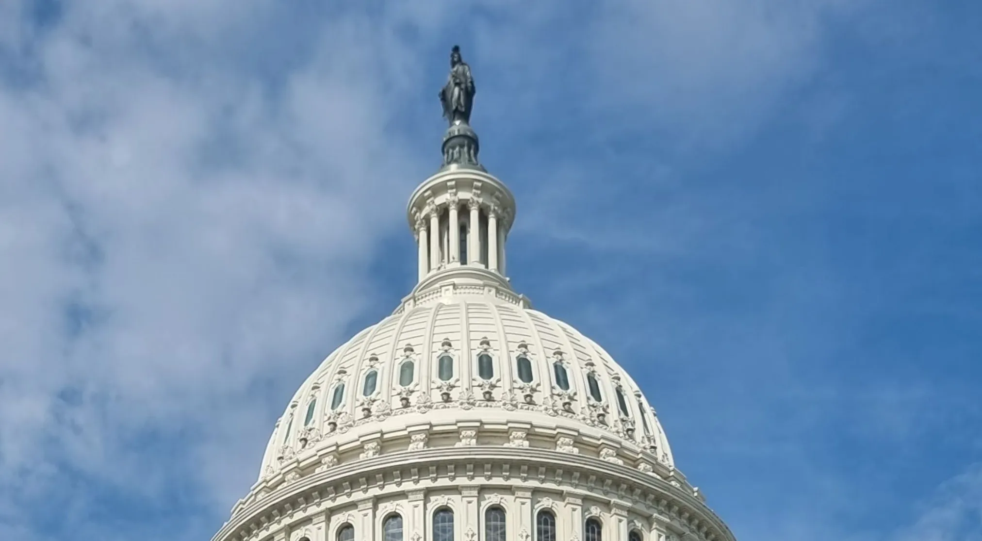 Zoomed in landmark: The US Capitol dome with the Statue of Freedom against a cloudy blue sky.