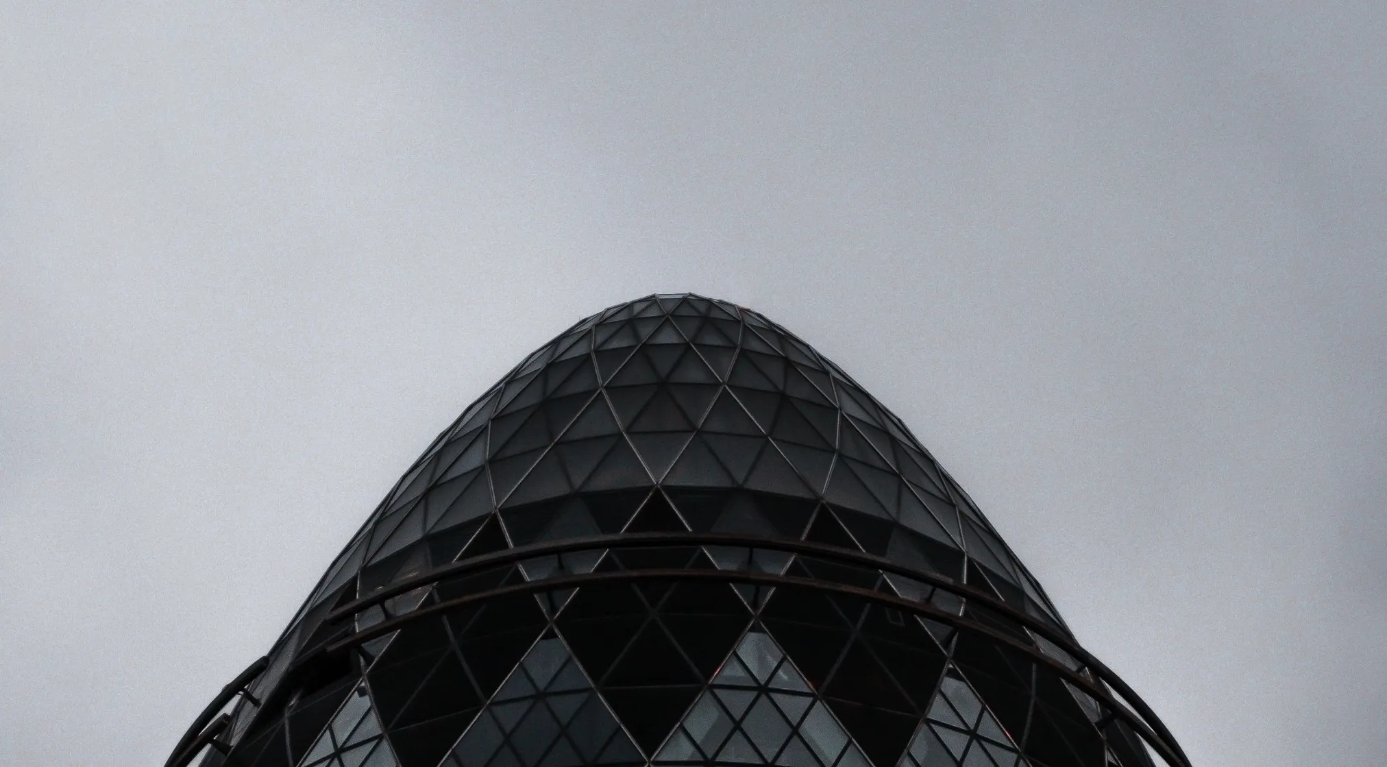 A close-up of a famous landmark, the Gherkin building's patterned glass dome against a gray sky. Zoomed in Landmarks.