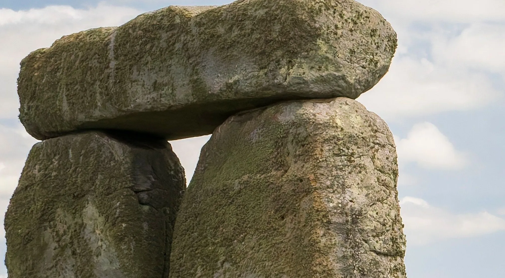 A zoomed-in image of three weathered, lichen-covered stones forming a structure under a cloudy sky. Can you recognize this landmark?