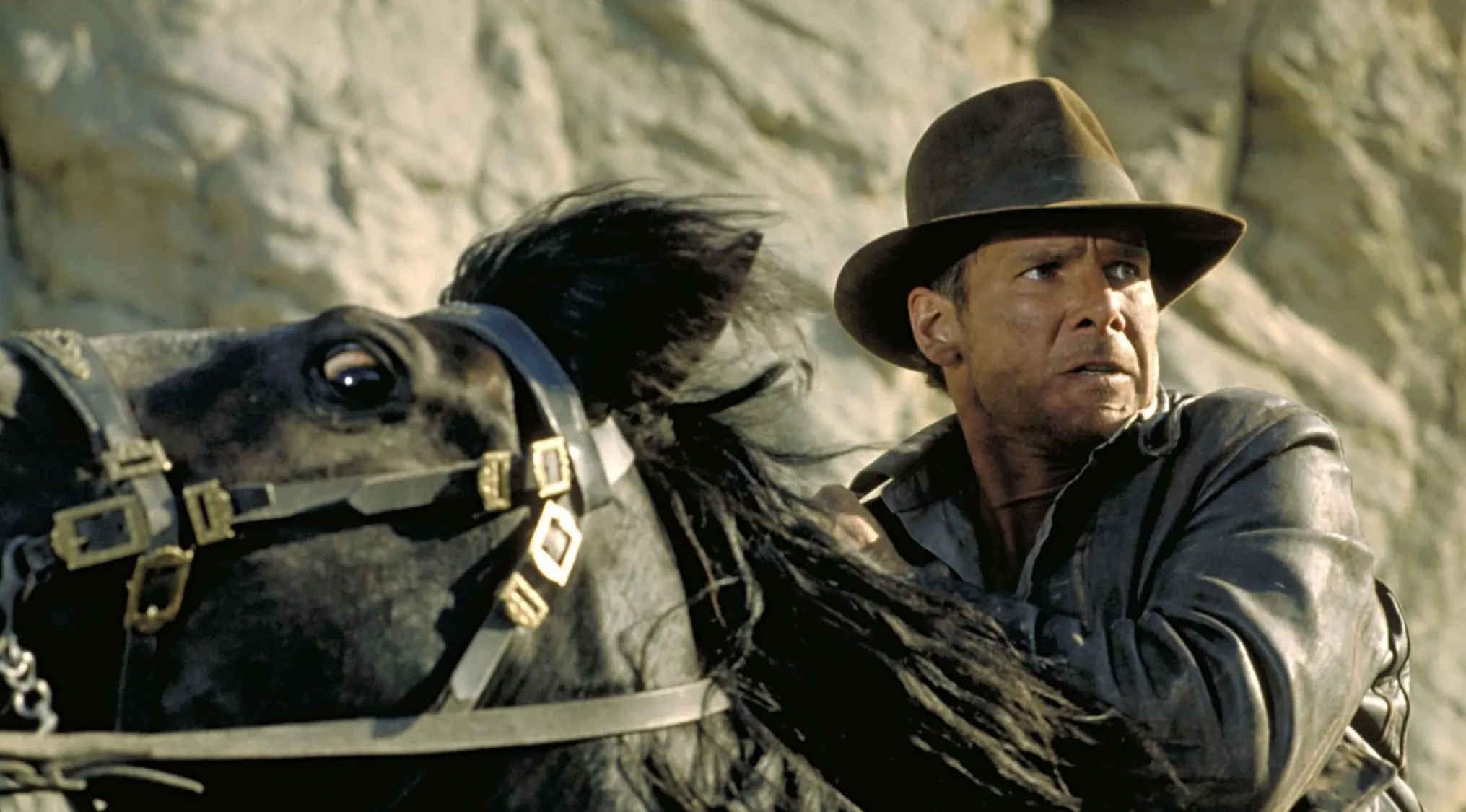 Harrison Ford as Indiana Jones riding a horse, an iconic movie franchises adventurer.