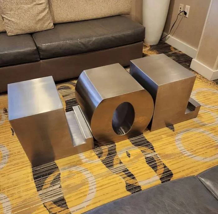 Three large, metallic silver letters spelling 'LOL' acting as bizarre furniture pieces or decorative elements in a room.