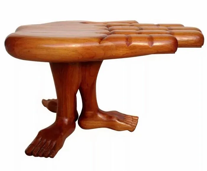 A unique wooden furniture design featuring a table top shaped like a giant hand supported by legs sculpted as human feet, showcasing bizarre furniture.