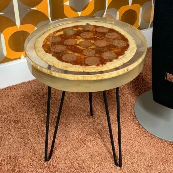 A round side table with a whole pepperoni pizza sealed under a clear surface, a bizarre furniture piece.