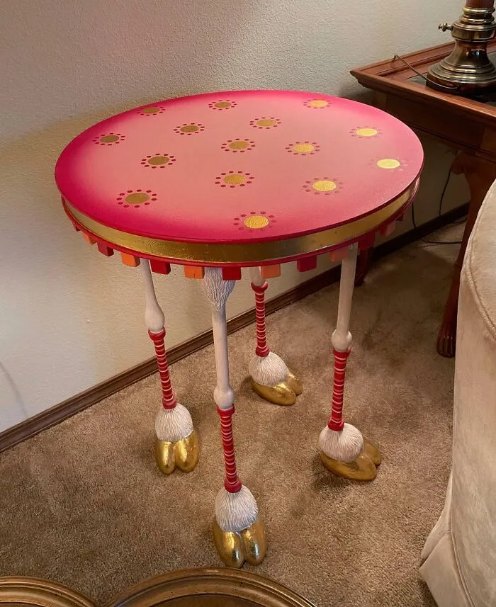 A round, pink table with golden polka dots and four animal-like legs with golden hooves, a bizarre furniture creation.