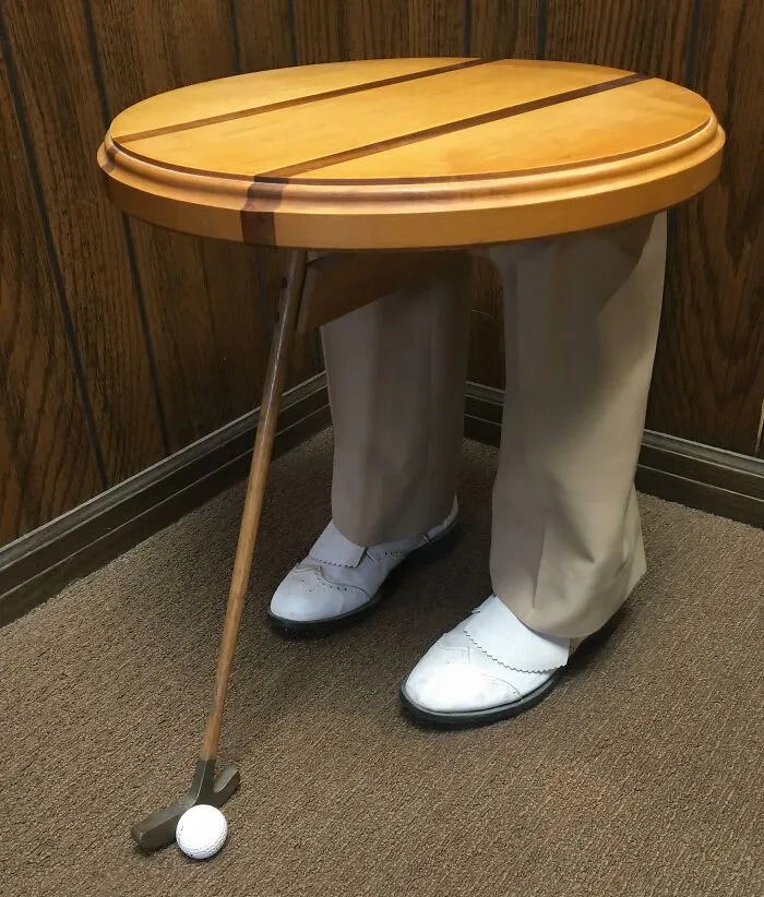An unusual round side table with furniture designers' golf-themed legs, showing khaki pants and a golf club.